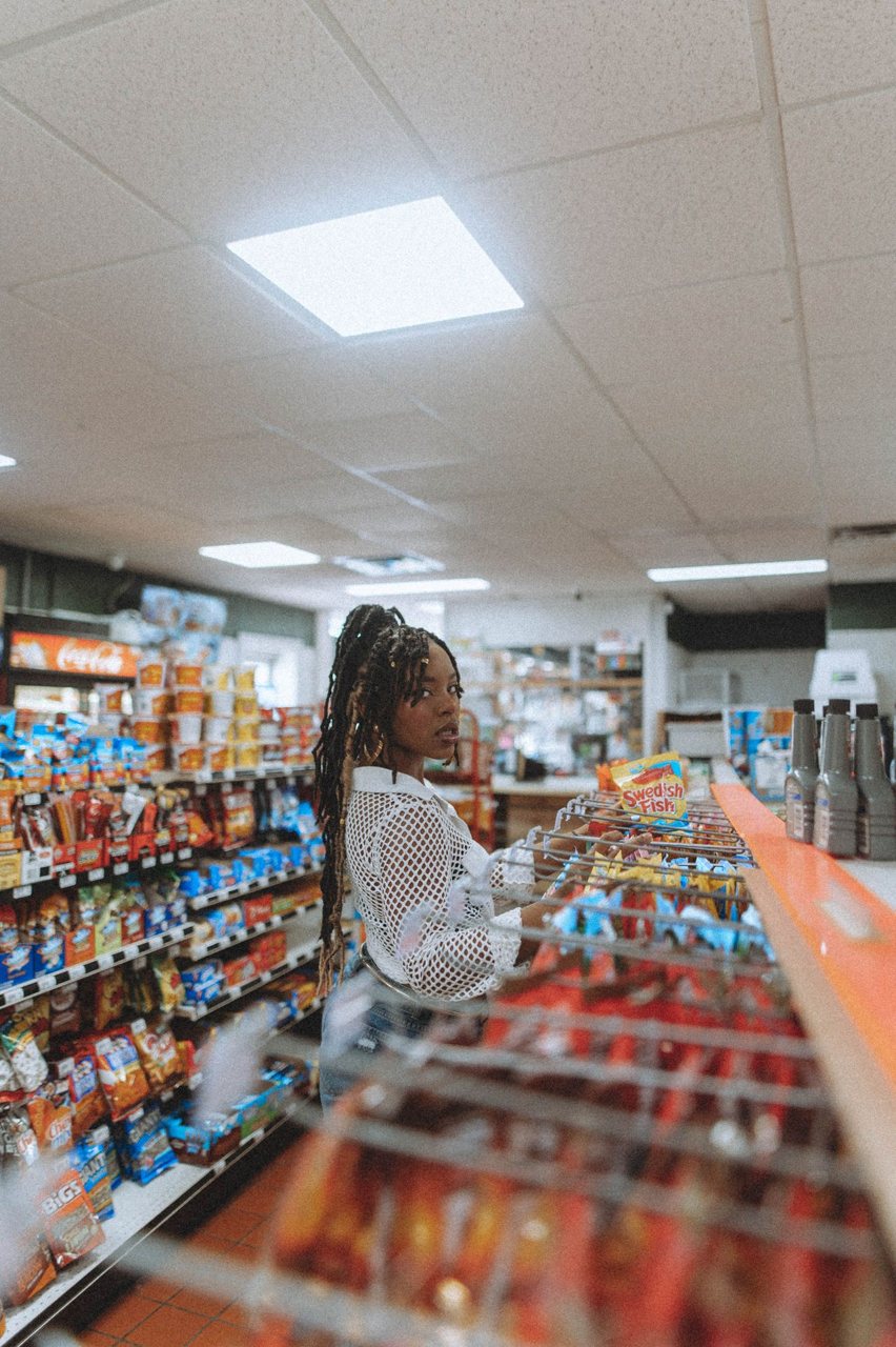 Free African American woman standing in a grocery store aisle, picking snacks. Indoor retail scene. Stock Photo